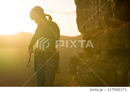 Young girl is preparing for training on the rocks sunset, in the mountains and puts a helmet Young girl is preparing for training on the rocks sunset, in the mountains and puts a helmet 127988171