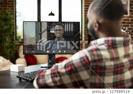 African american employee in home office speaking with company manager on video call, discussing marketing strategies and responsibilities. Virtual meeting showing teamwork in remote workspaces. African american employee in home office speaking with company manager on video call, discussing marketing strategies and responsibilities. Virtual meeting showing teamwork in remote workspaces. 127989519