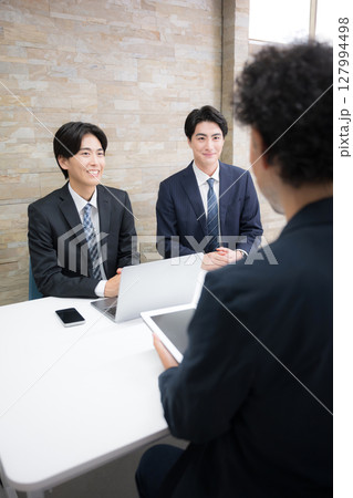 デスクでお客様に説明する若手の営業マン複数のイメージ ミーティングや打ち合わせなど デスクでお客様に説明する若手の営業マン複数のイメージ ミーティングや打ち合わせなど 127994498