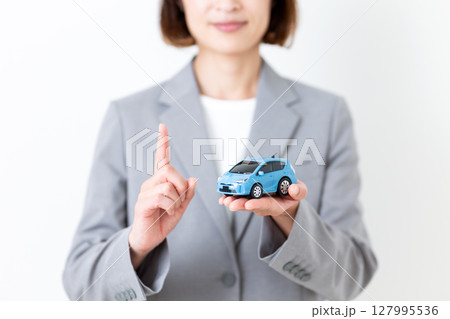 自動車の模型を持って人差し指を立てるグレーのスーツ姿のミドル女性 127995536