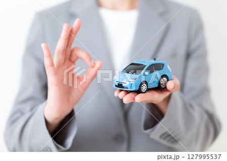 自動車の模型を持って丸サインをするグレーのスーツ姿のミドル女性 自動車の模型を持って丸サインをするグレーのスーツ姿のミドル女性 127995537