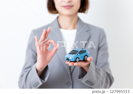 自動車の模型を持って丸サインをするグレーのスーツ姿のミドル女性 127995553