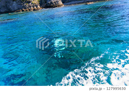 ヒリゾ浜渡船に乗って出港するスキンダイバー、シュノーケラー。 青い海と無人島の大根島、岩礁が見える。 127995630