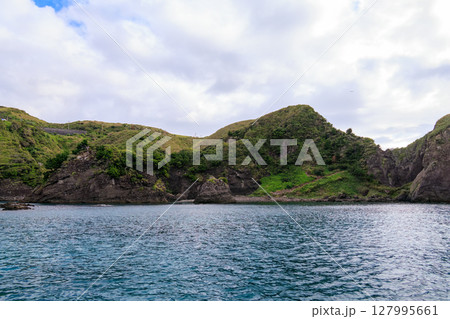 ヒリゾ浜渡船に乗って出港するスキンダイバー、シュノーケラー。 青い海と無人島の大根島、岩礁が見える。 127995661
