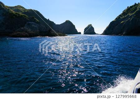 ヒリゾ浜渡船に乗って出港するスキンダイバー、シュノーケラー。 青い海と無人島の大根島、岩礁が見える。 127995668