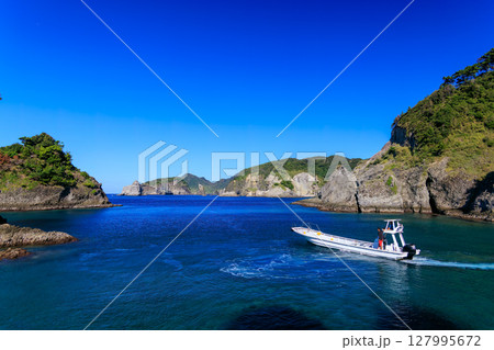 ヒリゾ浜渡船に乗って出港するスキンダイバー、シュノーケラー。 青い海と無人島の大根島、岩礁が見える。 127995672