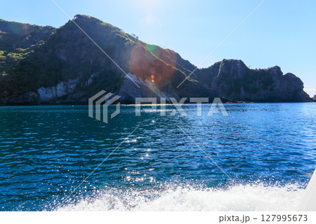 ヒリゾ浜渡船に乗って出港するスキンダイバー、シュノーケラー。 青い海と無人島の大根島、岩礁が見える。 127995673