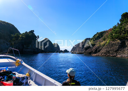ヒリゾ浜渡船に乗って出港するスキンダイバー、シュノーケラー。 青い海と無人島の大根島、岩礁が見える。 127995677