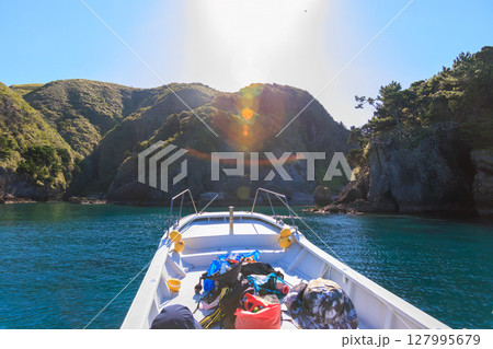 ヒリゾ浜渡船に乗って出港するスキンダイバー、シュノーケラー。 青い海と無人島の大根島、岩礁が見える。 127995679