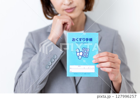 お薬手帳を持って悩むグレーのスーツ姿のミドル女性 127996257