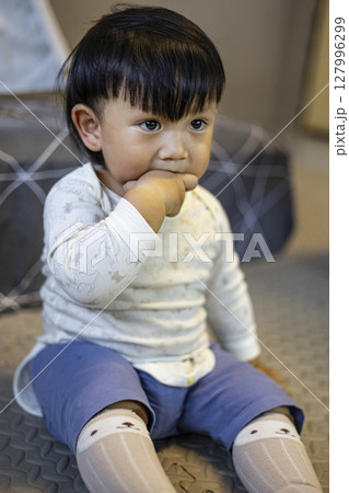 Toddler In Baby Suit Putting Fingers In Mouth, Background for advertising and wallpaper in education and lifestyle scene. Toddler In Baby Suit Putting Fingers In Mouth, Background for advertising and wallpaper in education and lifestyle scene. 127996299