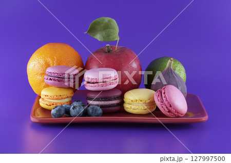 Vibrant scene of macarons and fruits over purple Vibrant scene of macarons and fruits over purple 127997500