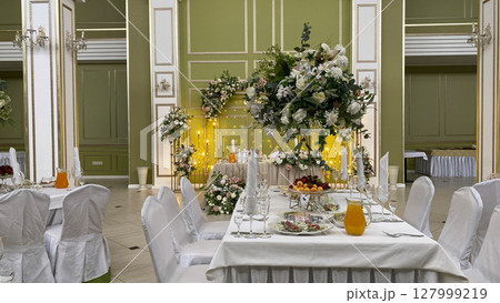 Elegant banquet hall with a beautifully decorated table featuring floral arrangements, crystal glasses, and a serene atmosphere. Perfect setting for a wedding, celebration, or special event Elegant banquet hall with a beautifully decorated table featuring floral arrangements, crystal glasses, and a serene atmosphere. Perfect setting for a wedding, celebration, or special event 127999219