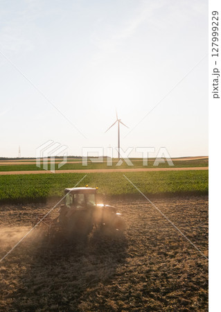 Agricultural tractor is working on the field with wind turbines. Aerial view. Agricultural tractor is working on the field with wind turbines. Aerial view. 127999229