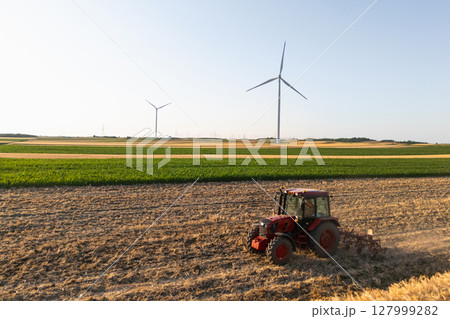 Agricultural tractor is working on the field with wind turbines. Aerial view. 127999282