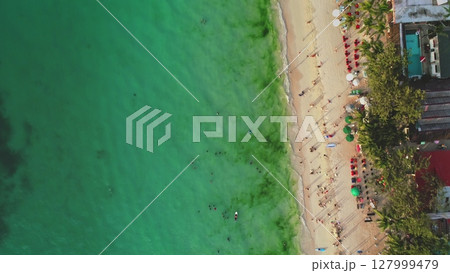 Aerial view of Cagban Beach in Boracay, Philippines, featuring tourists swimming in turquoise waters and sunbathing on the sandy shore under palm trees and umbrellas 127999479