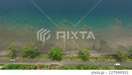 Fiji, Savu-Savu island: Aerial view of transparent shallow waters with rocks and corals alongside a coastal road, car driving countryside, lush vegetation, sunny day light. Aerial view drone footage 127999501