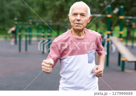 Active senior man is jogging in summer park. Healthy retirement lifestyle 127999889