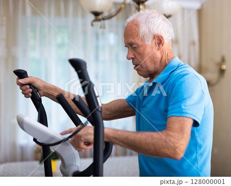 Old man using elliptic trainer at home 128000001