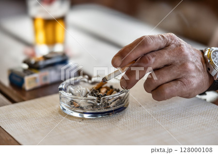 The hand of a smoking man or woman on a table led an ashtray with draft beer in a pub 128000108
