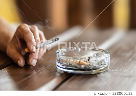 The hand of a smoking woman with a cigarette taps the ash into an ashtray The hand of a smoking woman with a cigarette taps the ash into an ashtray 128000112