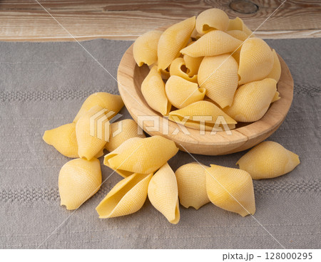 Raw conchiglioni pasta in wood bowl. Dry conchiglie noodle in shell shape 128000295
