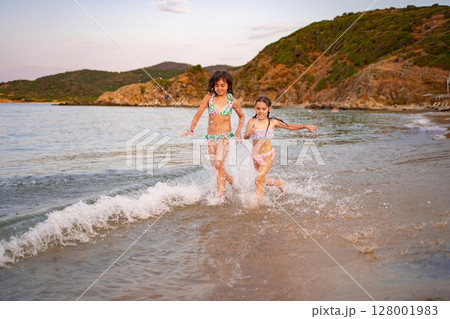 Joyful sisters splashing in the waves at a beautiful sunset beach 128001983