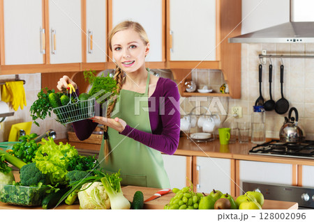 Woman in kitchen having vegetables holding shopping basket Woman in kitchen having vegetables holding shopping basket 128002096
