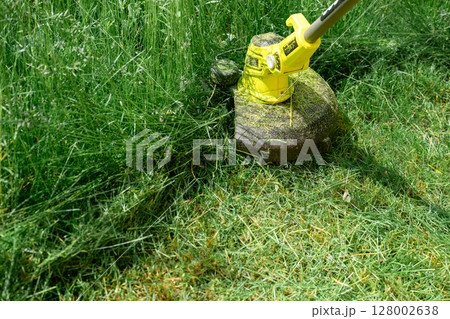 man trimming overgrown grass with electric string trimmer in summer garden 128002638