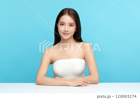 A beautiful young Asian woman with clean, fresh skin against a blue background. Skincare, facial treatment, cosmetology, beauty, and spa. An elegant portrait of an Asian woman. A beautiful young Asian woman with clean, fresh skin against a blue background. Skincare, facial treatment, cosmetology, beauty, and spa. An elegant portrait of an Asian woman. 128003274