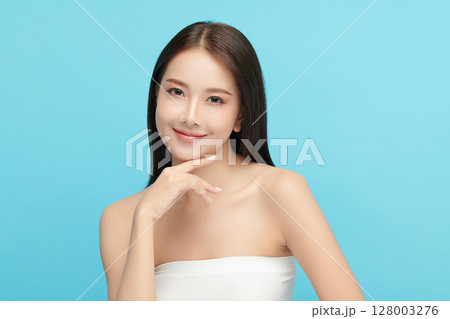 A beautiful young Asian woman with clean, fresh skin against a blue background. Skincare, facial treatment, cosmetology, beauty, and spa. An elegant portrait of an Asian woman. A beautiful young Asian woman with clean, fresh skin against a blue background. Skincare, facial treatment, cosmetology, beauty, and spa. An elegant portrait of an Asian woman. 128003276