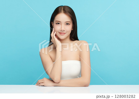 A beautiful young Asian woman with clean, fresh skin against a blue background. Skincare, facial treatment, cosmetology, beauty, and spa. An elegant portrait of an Asian woman. A beautiful young Asian woman with clean, fresh skin against a blue background. Skincare, facial treatment, cosmetology, beauty, and spa. An elegant portrait of an Asian woman. 128003282