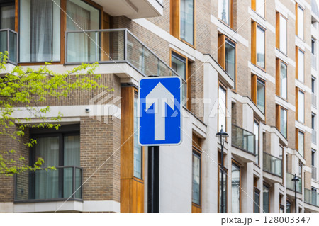 Blue one way traffic sign with upward arrow on modern city street near contemporary flats 128003347