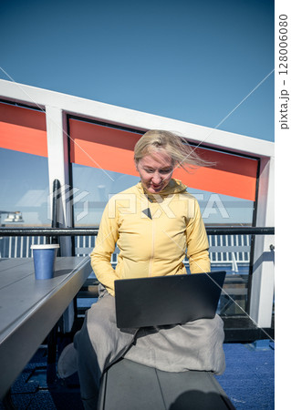 Woman working on laptop outdoors on ferry deck with coffee on sunny windy day Woman working on laptop outdoors on ferry deck with coffee on sunny windy day 128006080