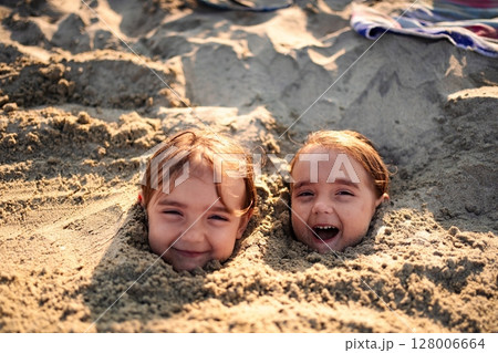 Sisters embrace summer fun with sandy smiles at the beach Sisters embrace summer fun with sandy smiles at the beach 128006664