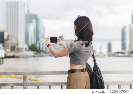Solo southeast asian woman teenager blogger take photo with smartphone and wait for boat. An express world travel explorer tourism concept for local cultural experience Chao Phraya river Bangkok 128007064