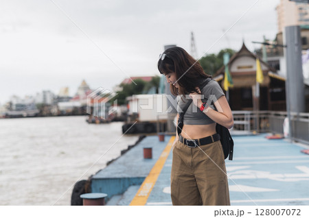 Solo southeast asian woman teenager blogger smartphone wait express boat friend Chao Phraya river Bangkok. World travel explorer tourism concept local cultural experience Thailand Asia Solo southeast asian woman teenager blogger smartphone wait express boat friend Chao Phraya river Bangkok. World travel explorer tourism concept local cultural experience Thailand Asia 128007072