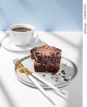 Chocolate brownie with nuts on a plate on a light background with cup of freshly brewed coffee Chocolate brownie with nuts on a plate on a light background with cup of freshly brewed coffee 128007931