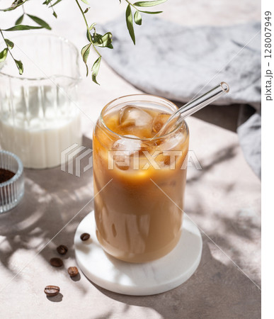 Ice latte coffee in a glass with milk on a light background with coffee beans and morning shadows. Ice latte coffee in a glass with milk on a light background with coffee beans and morning shadows. 128007949