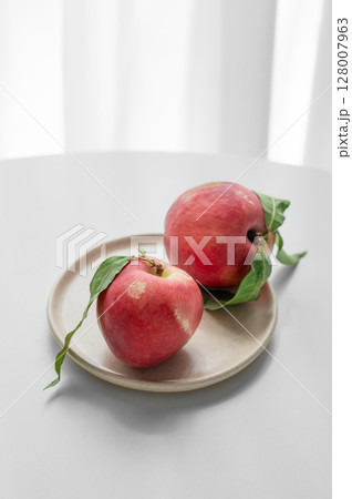 Fresh red peaches or nectarines with green leaves, on plate on white table and sunlight from window. 128007963
