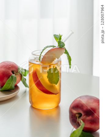 Ice tea with peach, mint in a glass on a white table near window with fresh fruits and sunlight. Ice tea with peach, mint in a glass on a white table near window with fresh fruits and sunlight. 128007964