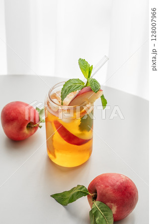 Ice tea with peach, mint in a glass on a white table near window with fresh fruits and sunlight. 128007966