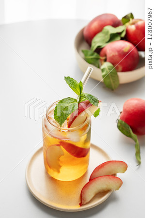 Ice tea with peach, mint in a glass on a white table near window with fresh fruits and sunlight. Ice tea with peach, mint in a glass on a white table near window with fresh fruits and sunlight. 128007967