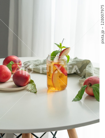 Ice tea with peach, mint in a glass on a white table near window with fresh fruits and sunlight. Ice tea with peach, mint in a glass on a white table near window with fresh fruits and sunlight. 128007975