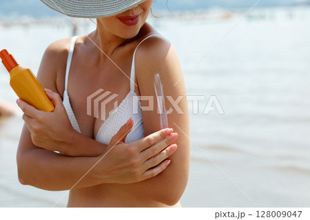 Woman Applying Sunscreen While Enjoying a Sunny Day at the Beach Woman Applying Sunscreen While Enjoying a Sunny Day at the Beach 128009047