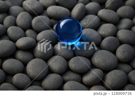 Vibrant blue glass sphere standing out on a pile of dark grey pebbles 128009716