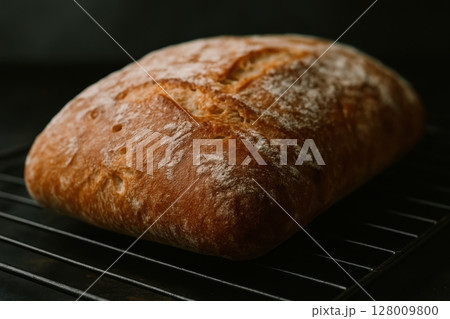 Golden brown rustic artisan bread loaf with crispy crust on a dark cooling rack Golden brown rustic artisan bread loaf with crispy crust on a dark cooling rack 128009800