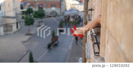 Close-up of female legs with red shoes of high heels. The woman is raising her feet through the window 128010202