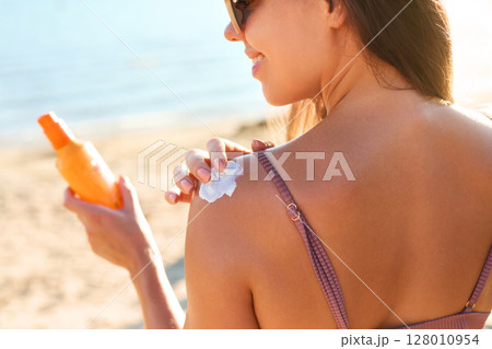 Skin care. Sun protection. Woman Applies Sunscreen on the Back. Woman With Suntan Lotion On Beach. Portrait of Female With Sun Cream on Shoulder. Girl Holding Moisturizing Sunblock Skin care. Sun protection. Woman Applies Sunscreen on the Back. Woman With Suntan Lotion On Beach. Portrait of Female With Sun Cream on Shoulder. Girl Holding Moisturizing Sunblock 128010954