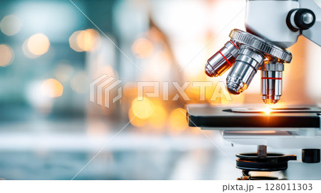 Close-up view of a modern microscope with multiple objective lenses, showcasing advanced technology in a laboratory setting with blurred background 128011303